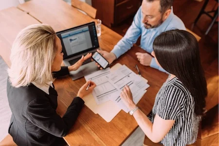 Adviser discussing SMSF pension strategy with two clients reviewing property and cashflow documents at a table