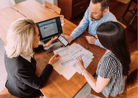 Adviser discussing SMSF pension strategy with two clients reviewing property and cashflow documents at a table