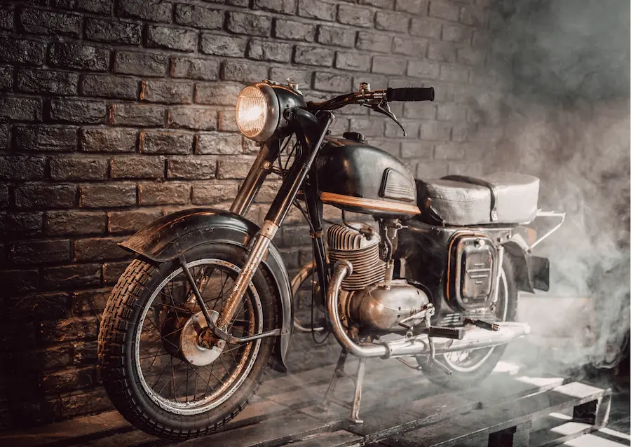 Vintage motorcycle displayed indoors against a brick wall with atmospheric smoke, example of a collectable asset under SMSF rules
