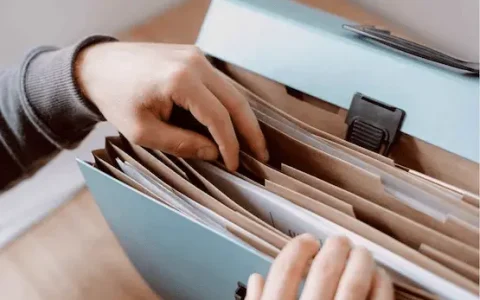 Person sorting through paper files in a folder, representing careful SMSF compliance and LRBA reporting for accurate TSB calculations